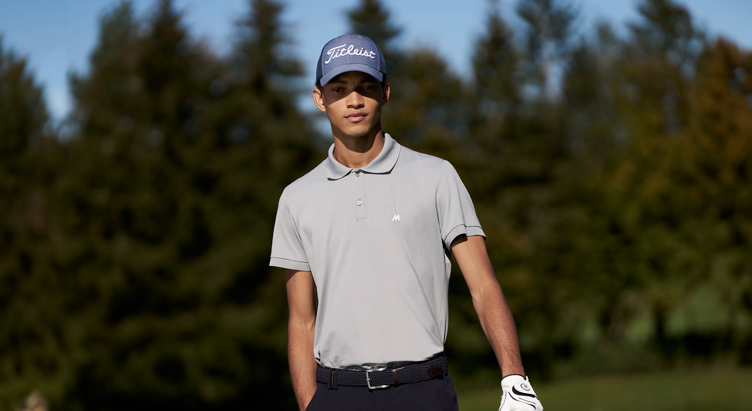 Person wearing a gray polo shirt and blue cap on a golf course with trees in the background